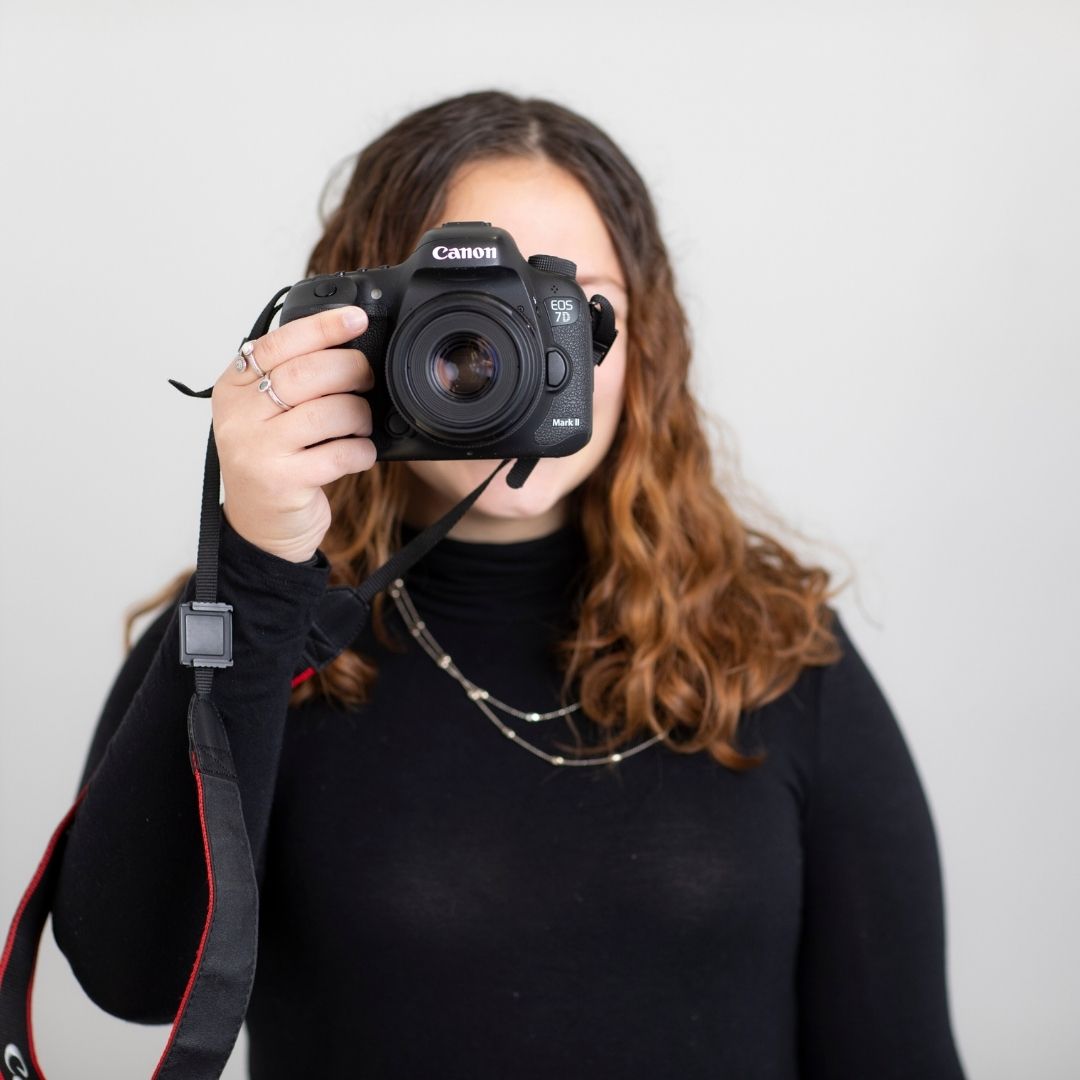 Jillian Lawrence holding a Canon camera in front of her face, showcasing her photography expertise.